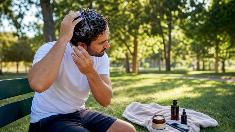 Un uomo si prende cura dei suoi ricci applicando una crema modellante davanti allo specchio del bagno.