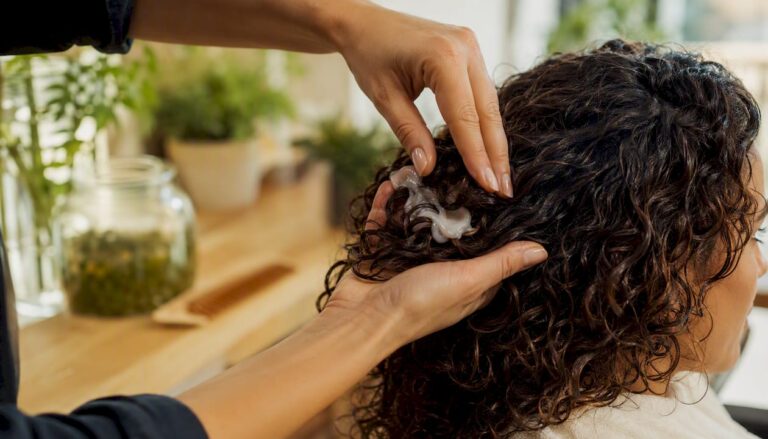 Mani che stendono una crema naturale tra i ricci, per nutrire e valorizzare la chioma.