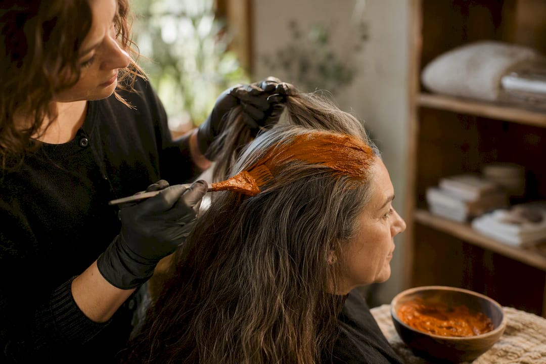 Mani che stendono la pasta di henné sui capelli grigi